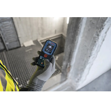 Hand mit Handschuh hält ein Bosch Entfernungsmessgerät in einem Rohbau.