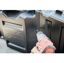 Ein Mann bohrt ein Loch in eine schwarze Huber Regentonne.