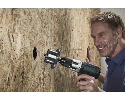 Ein Mann bohrt mit einer Lochsäge ein Loch in eine Holzplatte.