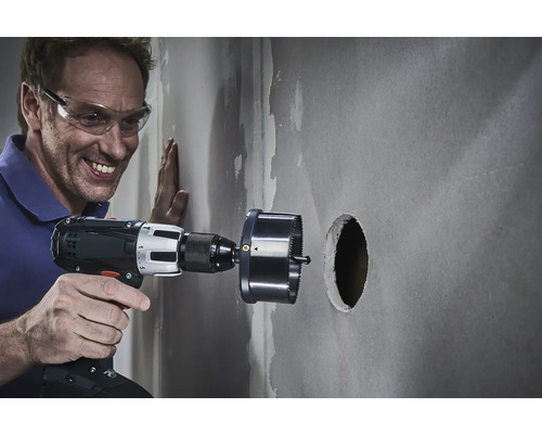 Mann bohrt mit einer Lochsäge ein Loch in eine Wand