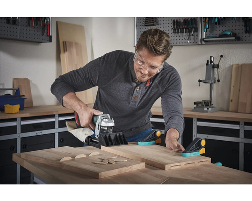 Ein Mann benutzt eine Dübelfräse in einer Werkstatt, um Holzteile zu bearbeiten.