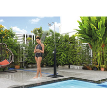 Frau unter einer Gartendusche im Außenbereich neben einem Pool.