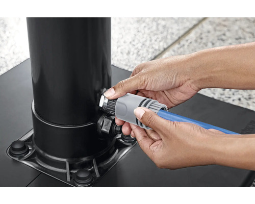 Eine Person schließt einen Gartenschlauch an einen Sonnenschirmständer an.