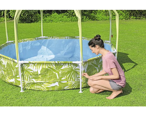 Aufbau eines runden Stahlrahmenpools mit Blätterdesign und Sonnendach im Garten.