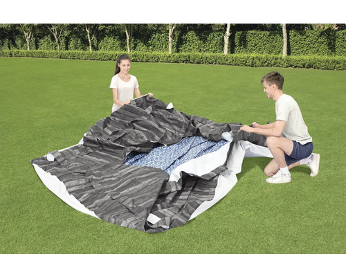 Personen bauen eine Poolabdeckung auf einer Rasenfläche auf.