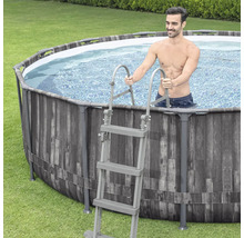 Aufstellpool mit Holzverkleidung und Leiter auf Rasen mit Mann im Pool