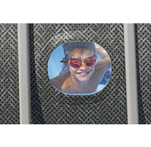 Lächelnder Junge mit Schwimmbrille unter Wasser, aufgenommen durch eine Poolluke