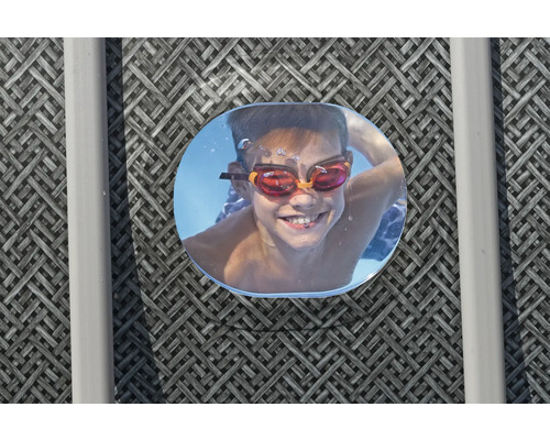 Lächelnder Junge mit Schwimmbrille unter Wasser, aufgenommen durch eine Poolluke