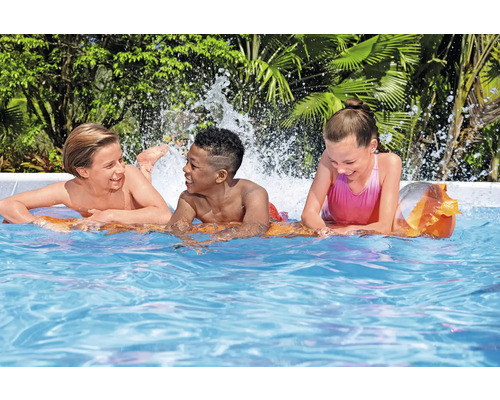 Drei Kinder spielen auf einer Luftmatratze im Schwimmbad.