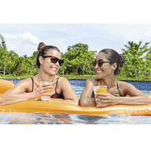 Zwei Frauen entspannen mit Getränken auf einer Luftmatratze im Schwimmbad.