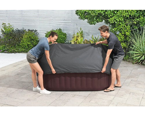 Zwei Personen legen eine Abdeckung über einen aufblasbaren Whirlpool im Freien.