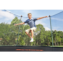 Junge springt auf einem Gartentrampolin mit Sicherheitsnetz vor Bäumen
