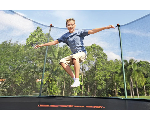 Junge springt auf einem Gartentrampolin mit Sicherheitsnetz vor Bäumen