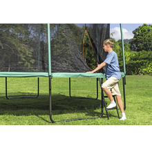 Junge steigt auf einer Leiter zu einem Gartentrampolin mit Sicherheitsnetz hoch.
