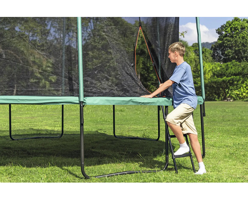 Junge steigt auf einer Leiter zu einem Gartentrampolin mit Sicherheitsnetz hoch.