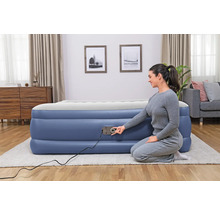 Frau bedient eine blaue Luftmatratze mit integrierter Pumpe in einem Wohnzimmer.