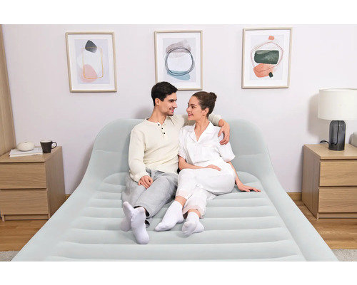 Paar sitzt auf einem hellen Luftbett mit Kopfteil in einem hellen, modernen Schlafzimmer