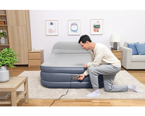 Mann pumpt Luftmatratze mit integrierter Pumpe in einem Wohnzimmer auf