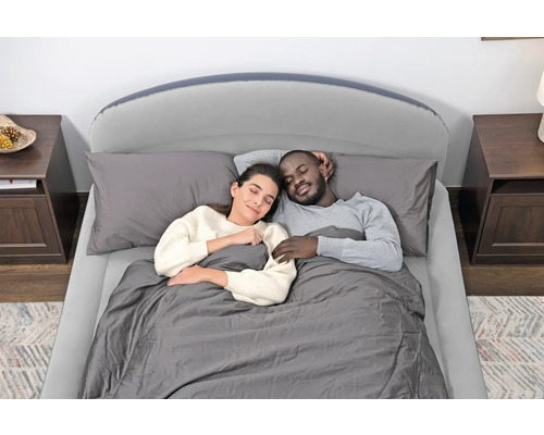 Paar schläft in einem Bett mit Lattenrost, Matratze, Kissen und Bettdecke.