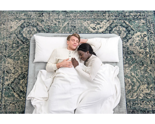 Paar schläft auf Bett mit Kissen und Decke auf gemustertem Teppich