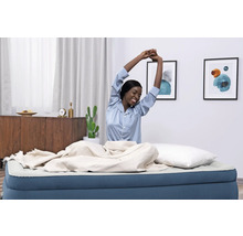 Frau dehnt sich auf Luftmatratze mit Decke und Kissen in einem hellen Raum.