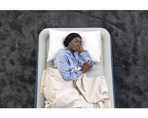 Luftmatratze mit schlafender Person, Kissen und Decke auf einem Teppich