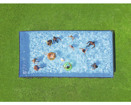 Draufsicht auf einen rechteckigen Pool mit mehreren Personen, Schwimmringen und einem Ball auf einer grünen Rasenfläche.