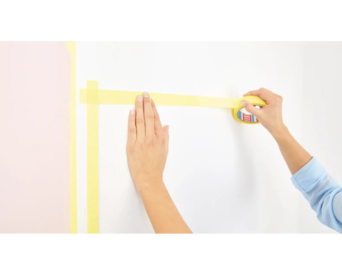 Eine Person klebt Malerkrepp an eine Wand.