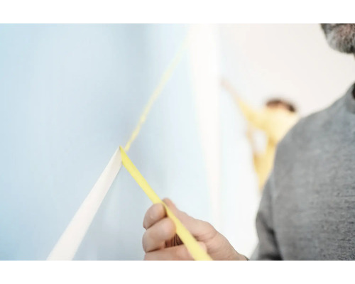 Mann befestigt Malerkrepp an einer Wand