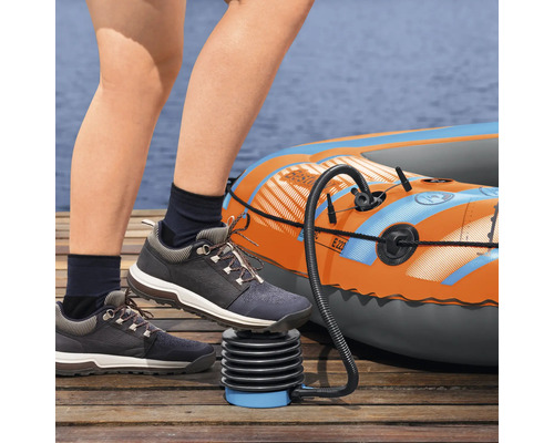 Person pumpt ein Schlauchboot mit einer Fußpumpe auf einem Holzsteg auf.