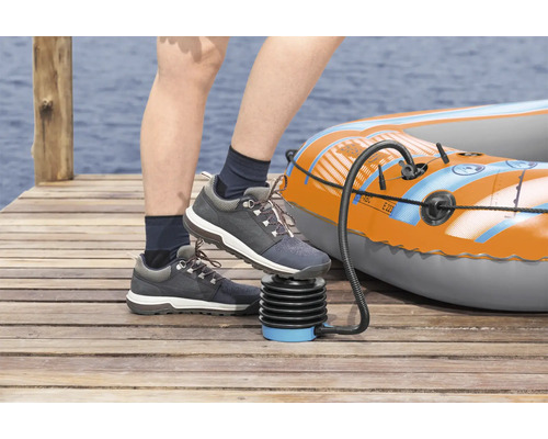 Person pumpt ein aufblasbares Boot mit einer Fußpumpe auf einem Holzsteg auf.