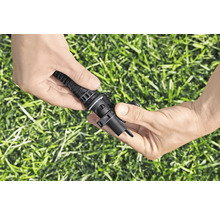 Hände verbinden ein Bewässerungsrohr mit einem Tropfer zur Gartenbewässerung