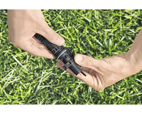 Hände verbinden ein Bewässerungsrohr mit einem Tropfer zur Gartenbewässerung
