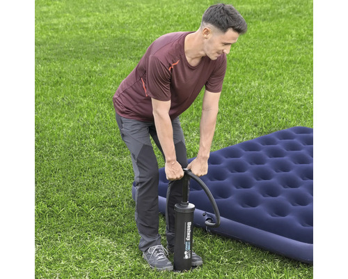 Mann pumpt Luftmatratze mit Luftpumpe auf Rasen auf