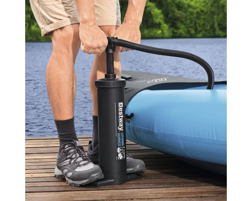 Person pumpt ein aufblasbares Kajak mit einer Handpumpe auf einem Holzsteg am See auf