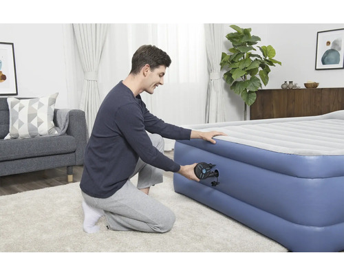 Mann pumpt Luftmatratze im Wohnzimmer auf.