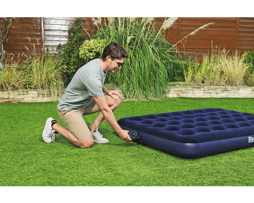 Ein Mann pumpt eine blaue Luftmatratze im Garten auf