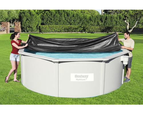 Personen decken ein rundes Schwimmbecken mit einer Poolabdeckung ab.