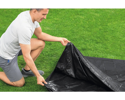 Eine Person verlegt eine schwarze Baufolie auf einer Rasenfläche.