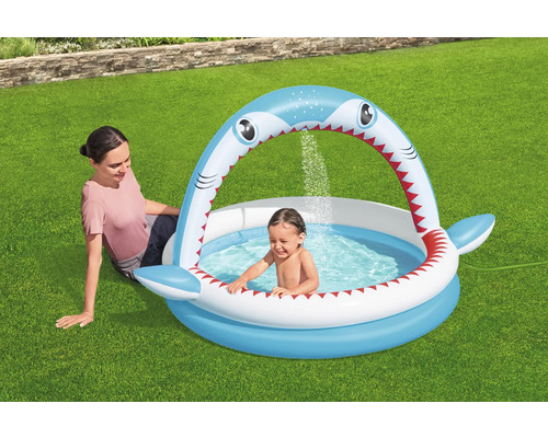 Aufblasbares Planschbecken in Haiform mit spielendem Kind und sitzender Frau im Garten.