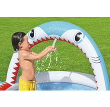 Kind spielt im aufblasbaren Planschbecken mit Hai-Design und Wassersprinklerfunktion im Garten.