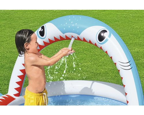 Kind spielt im aufblasbaren Planschbecken mit Hai-Design und Wassersprinklerfunktion im Garten.