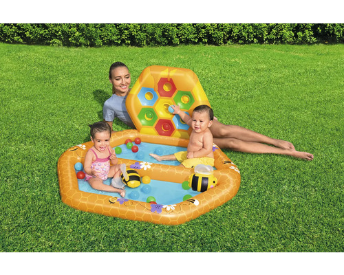 Aufblasbares Planschbecken mit Bienen-Design, Bällen und Spielwand auf einer Rasenfläche mit spielenden Kindern und einer Frau