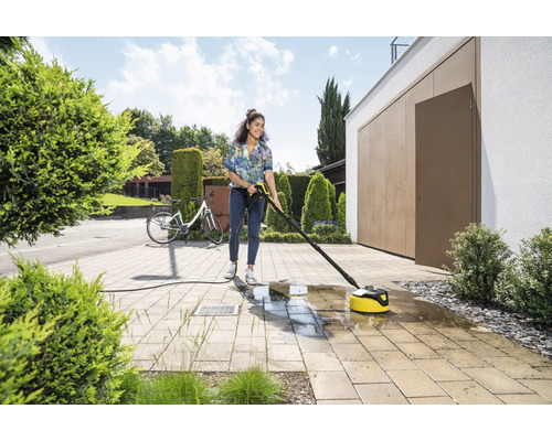 Frau reinigt Pflastersteine mit einem Terrassenreiniger von Kärcher vor einem Haus.