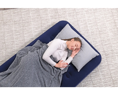 Frau schläft auf einer blauen Luftmatratze mit Kissen und Decke auf einem Teppich.