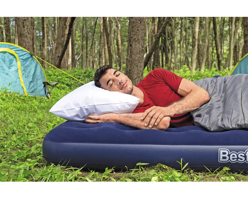 Mann schläft auf einer Luftmatratze mit Schlafsack und Kissen beim Camping