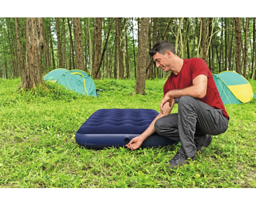 Mann pumpt eine Luftmatratze auf einem Campingplatz auf
