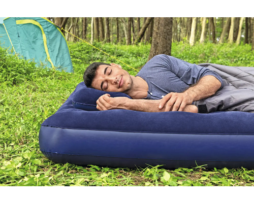 Mann schläft auf Luftmatratze mit Kissen und Schlafsack im Freien vor einem Zelt.