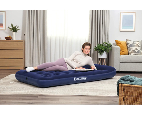 Frau liest auf einer blauen Bestway Luftmatratze im Wohnzimmer.
