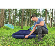 Mann bereitet eine Luftmatratze zum Campen vor dem Zelt vor.